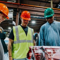 Three students wearing hard hats look at a miece of equipment. 