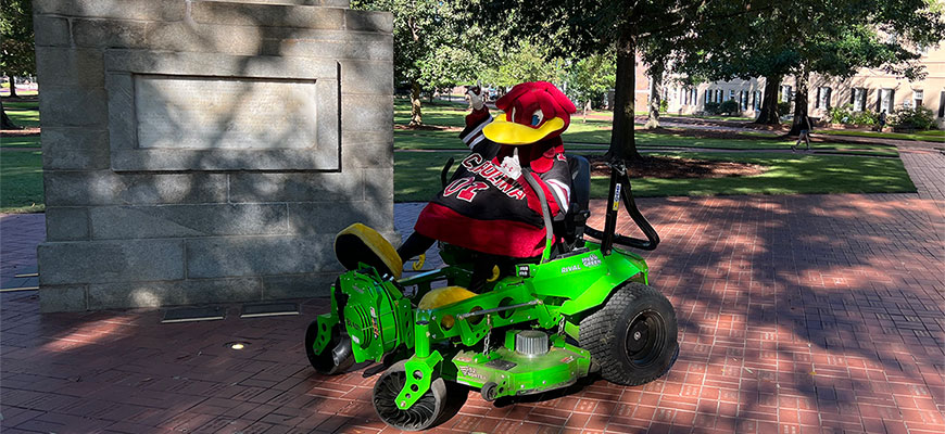 Cocky sitting on the new green machine mower in front of Maxcy Monument