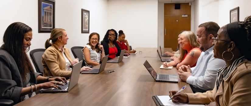 people sitting around a conference room table with laptops 