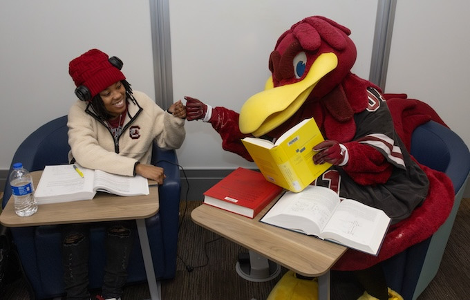 Cocky and student sitting in library and fist bumping