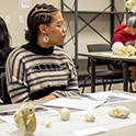 A student of color with braided hair sits at a lab table with various 3-D printed specimens.