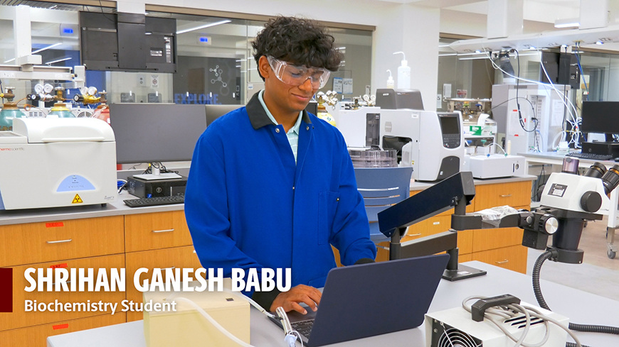 Shrihan Ganesh Babu, biochemistry student, stands at a computer in a lab setting.