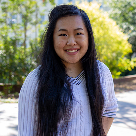 Psychology student Wendy Chu stands in a brick courtyard with trees and buildings in the background.