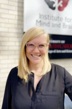 Jessica Bradshaw is smiling while wearing a black top posed in front of a white brick background