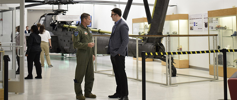 two men stand in front of the Apache helicopter in the McNair Center