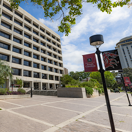 Exterior of the University of South Carolina’s Close-Hipp Building in Columbia, with trees, landscaped grounds and Gamecock banners lining the sidewalk.
