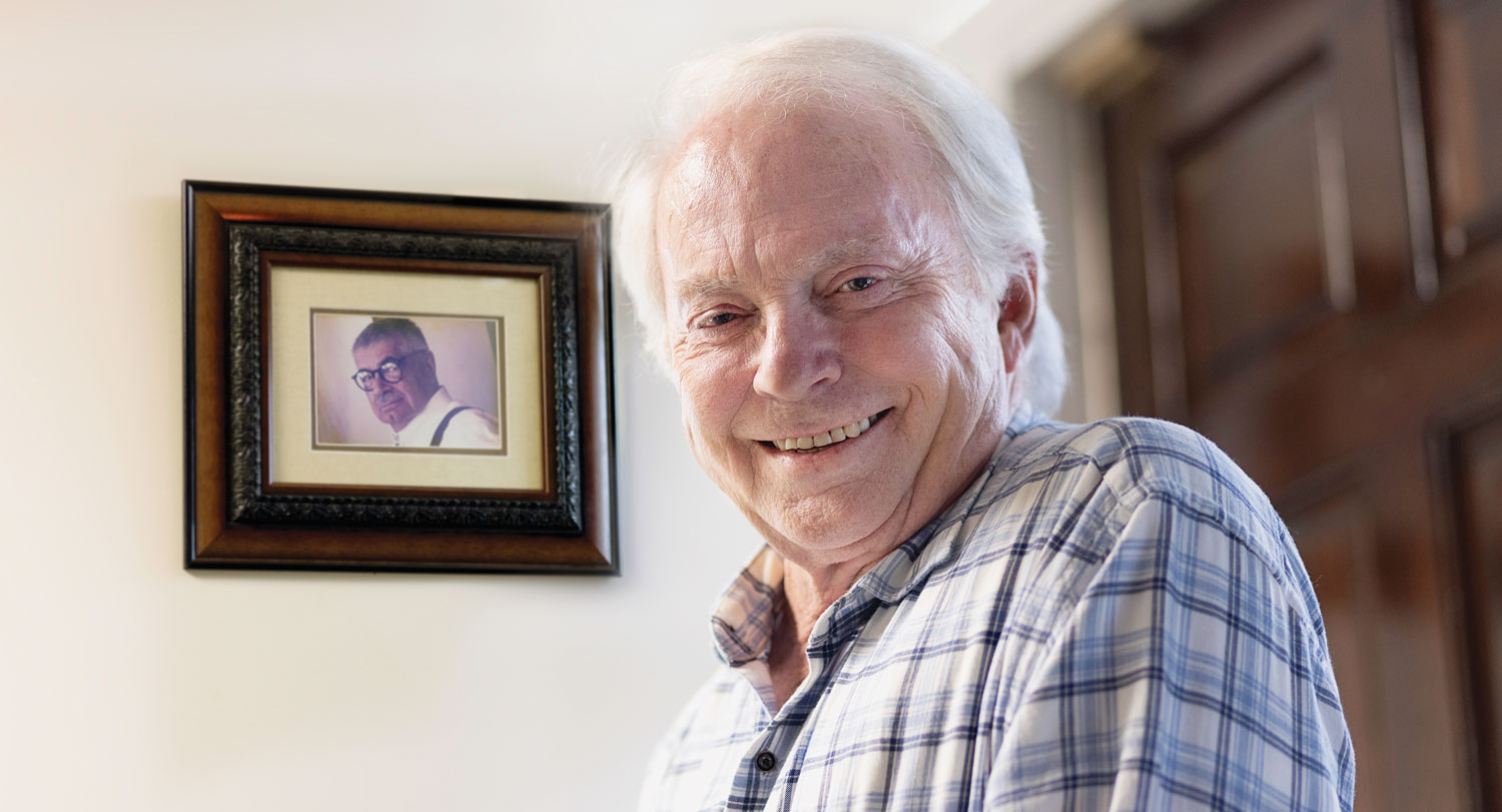 Rick Layman smiles for the camera with a photo of Dr. Matt Bruccoli in the background