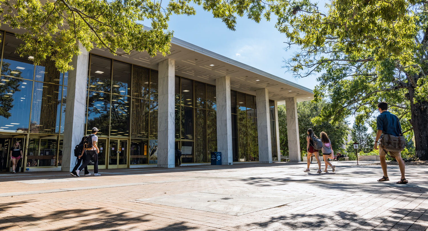 students walk into a building with large columns and glass walls