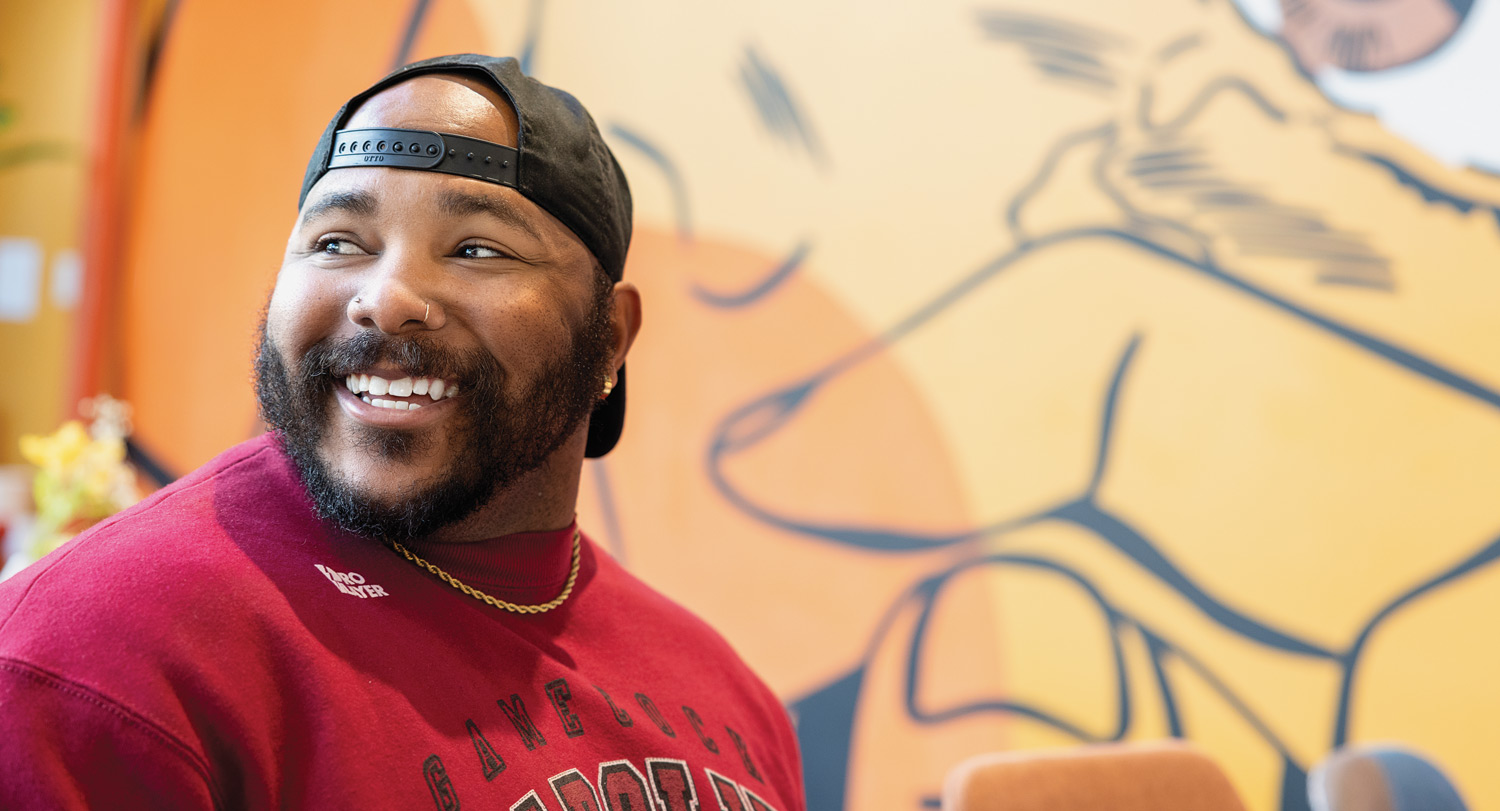 Garrison Gist smiles in front of a detail of his mural at Uptown Yolk, Charlotte, NC.