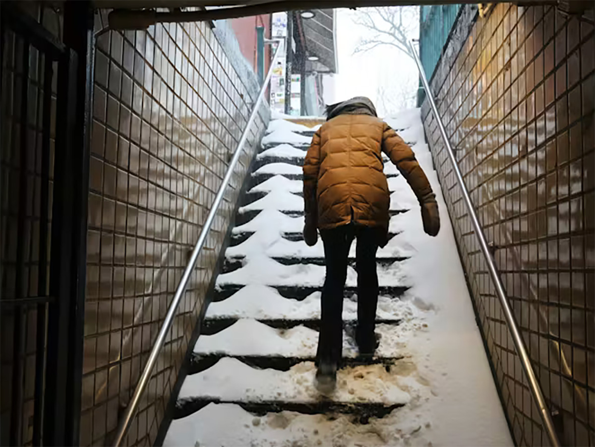 A man walks up snow-covered stairs out of a subway station.