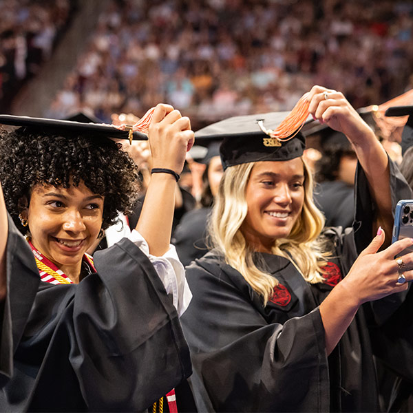 Two women in caps and gowns turning tassles on graduation caps