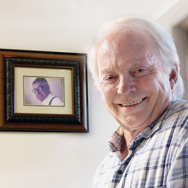 Rick Layman smiles for the camera with Matt Bruccoli’s photo in the background