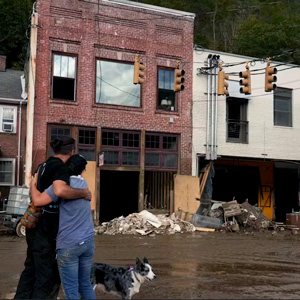 man and woman embrace while looking at flooded buildings