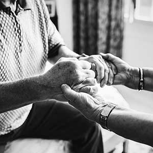 Female social worker holds hands of elderly male. 